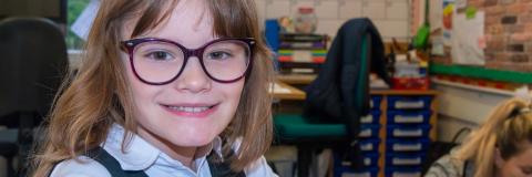 Bespectacled young girl in a classroom setting smiles for the camera