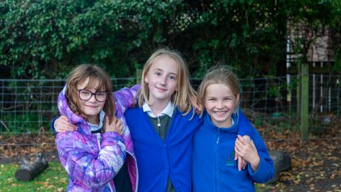 Three girls in the playground pose for a photograph