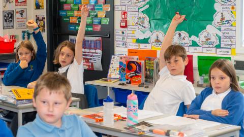 Pupils in a classroom setting with their hands in the air
